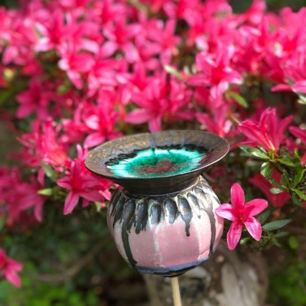 Pink ceramic poppy seed head among pink flowering azalea