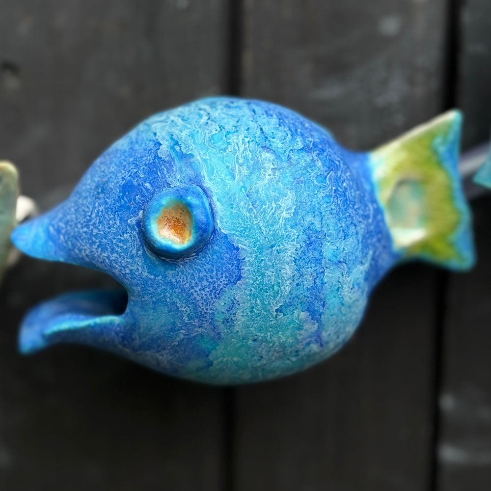 Blue fish as part of the fish-catcher; Wall hanging art: 5 ceramic fish assembled on a metal hoop with decorative scroll