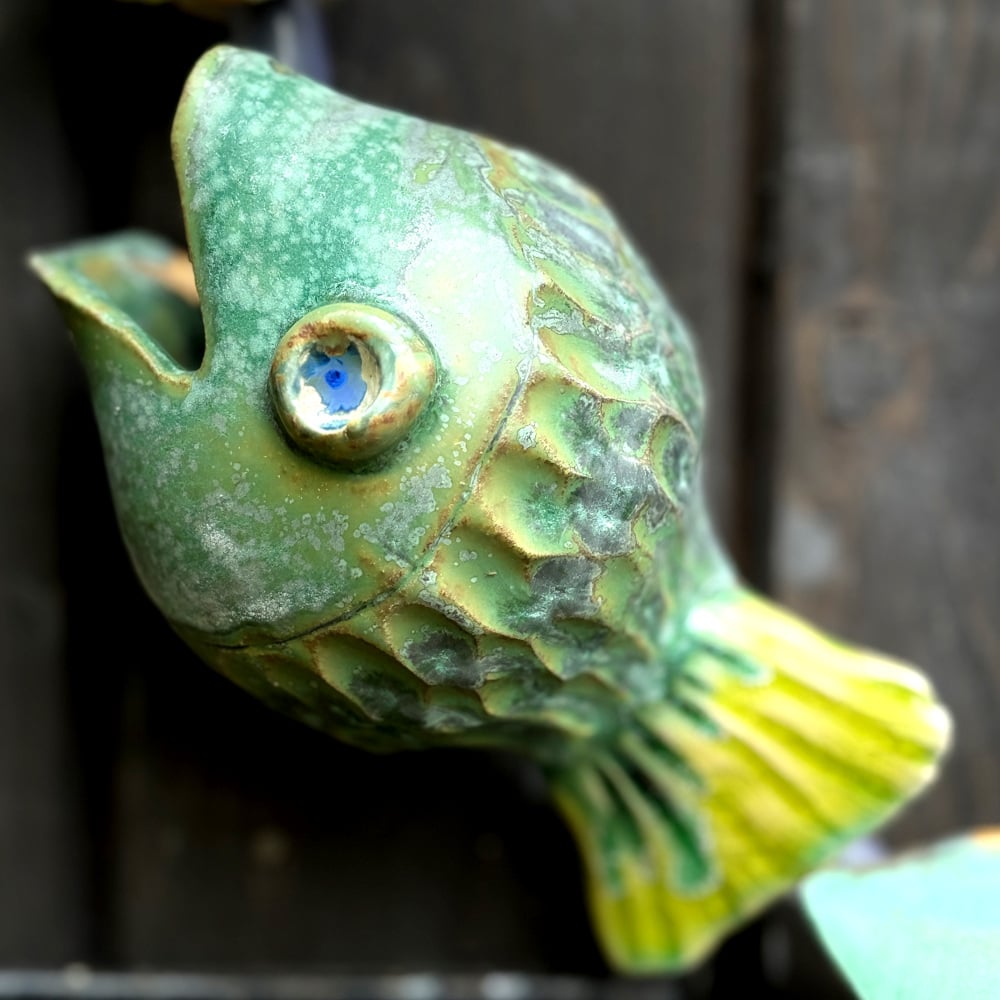 Green fish as part of the fish-catcher; Wall hanging art: 5 ceramic fish assembled on a metal hoop with decorative scroll